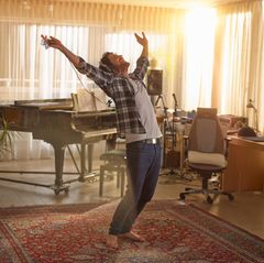 Ein Mann steht in einem Wohnzimmerähnlichen Studio mit Kopfhörern vor einem Klavier und tanzt
