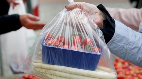 Spargel und Erdbeeren in der Verpackung werden über den Verkaufsstand gereicht.