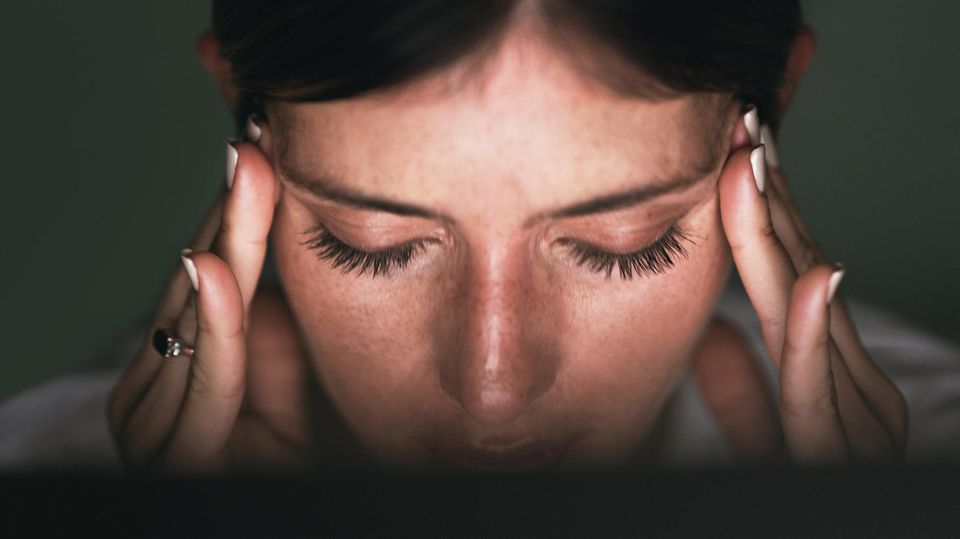 Erschöpfung erkennen, Burnout verhindern: Eine Frau fasst sich an den Kopf, sie wirkt gestresst