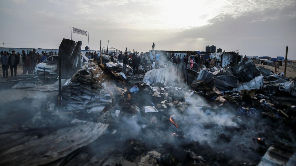 Menschen stehen vor einem brennenden und zerstörten Zeltlager in Rafah im Gazastreifen