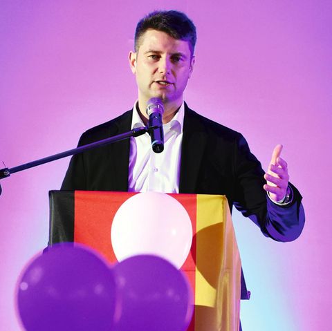 AfD-Politiker René Aust spricht an einem Podium mit Deutschlandfahne in ein Mikrofon
