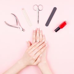 Nagelfeile Handgepäck: Gepflegte Hände und ein Manikür-Set liegen auf einem rosa Tisch.