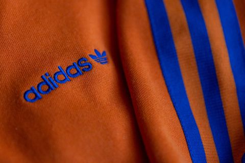 Das Logo des Sportartikelherstellers adidas in blau auf einer orangen Jacke