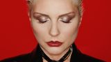 Debbie Harry vor rotem Hintergrund mit strenger Frisur und geschlossenen Augen
