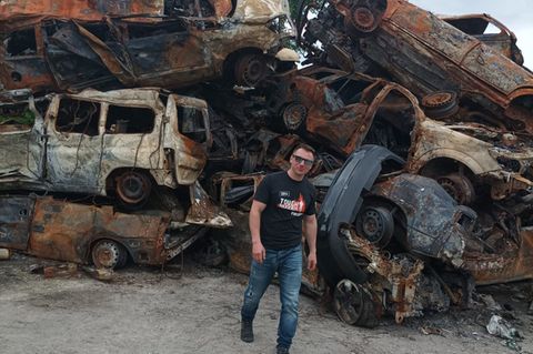 Reiseführer Svet Moiseev vor den Trümmern von im Krieg zerstörter Autos bei Kiew