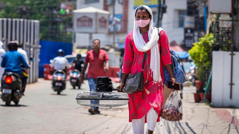 Indien: Eine Frau trägt einen Ventilator, den sie an einem heißen Sommertag auf einem Markt gekauft hat