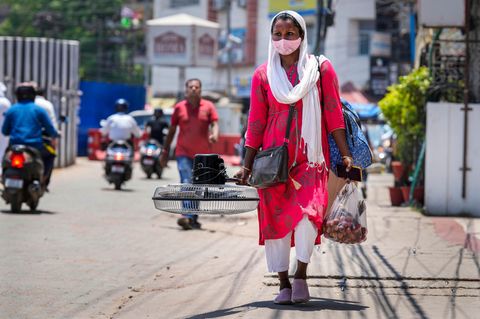 Indien: Eine Frau trägt einen Ventilator, den sie an einem heißen Sommertag auf einem Markt gekauft hat