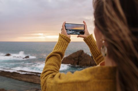 Smartphone-Fotografie: Die ultimativen Tipps. Frau fotografiert Sonnenuntergang am Meer.