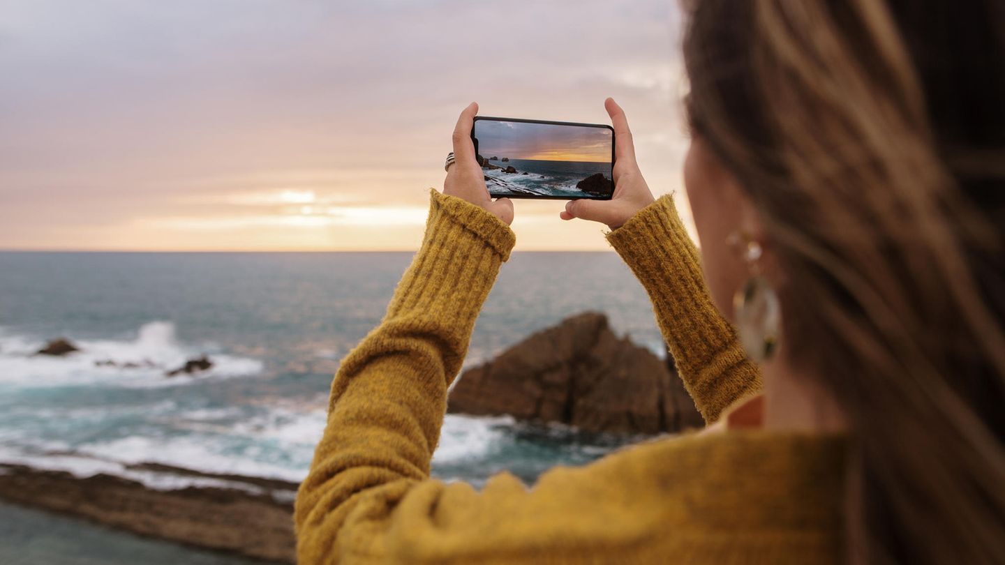 Smartphone-Fotografie: Die ultimativen Tipps. Frau fotografiert Sonnenuntergang am Meer.