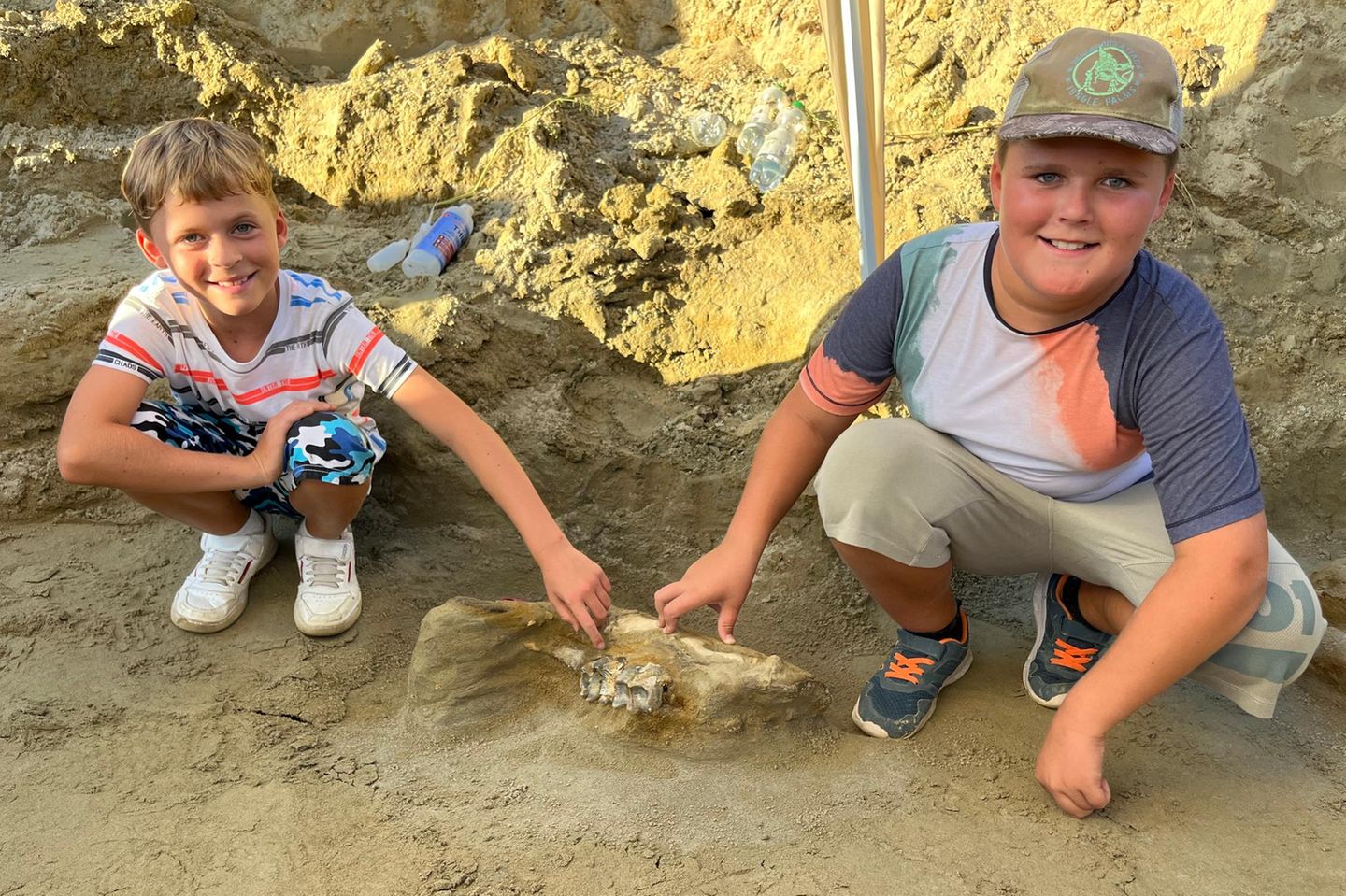 Constantin und Alexander Kapustin mit Knochen eines Urelefanten Zwei Jungen hocken in einer Sandgrube und zeigen auf einen Unterkiefer-Knochen