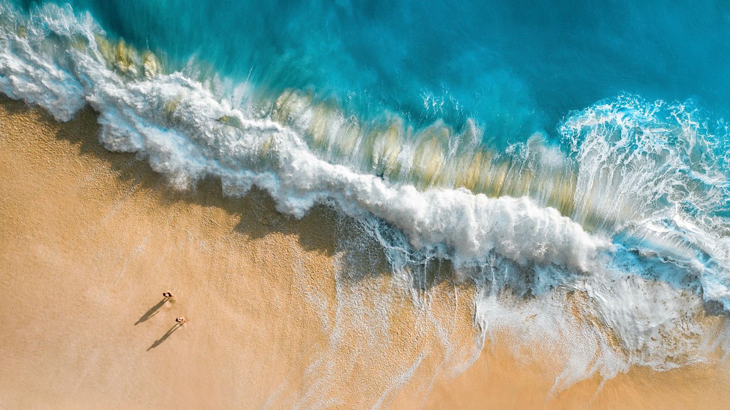Sommerurlaub Ein Pärchen läuft am Strand in Bali hohe wellen spülen durch den Sand