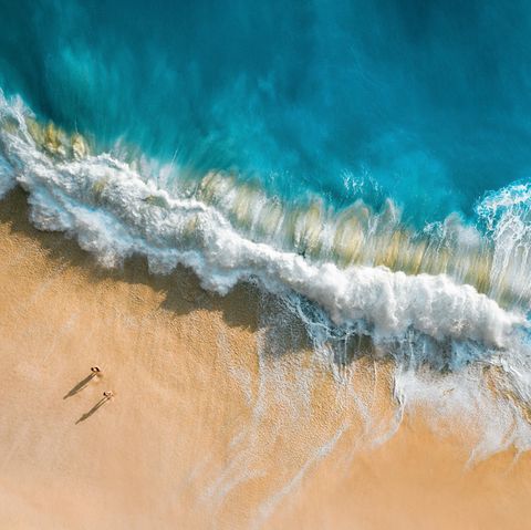 Ein Pärchen läuft am Strand in Bali hohe wellen spülen durch den Sand