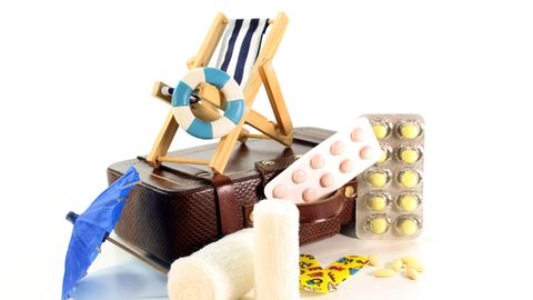 In einem Miniaturarrangement liegen Pillenpackungen neben einem Koffer, der naturheilkundlichen Reiseapotheke.