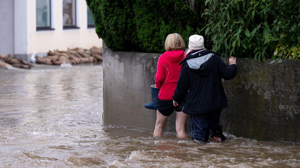In Reichertshofen gehen zwei Frauen eine überflutete Straße entlang. Es hat wie aus Eimern schüttet. Seit Freitagabend dauert der Kampf gegen die Fluten an – und am Sonntag ist noch kein Ende in Sicht. Vielerorts steigen die Pegelstände weiter dramatisch an.