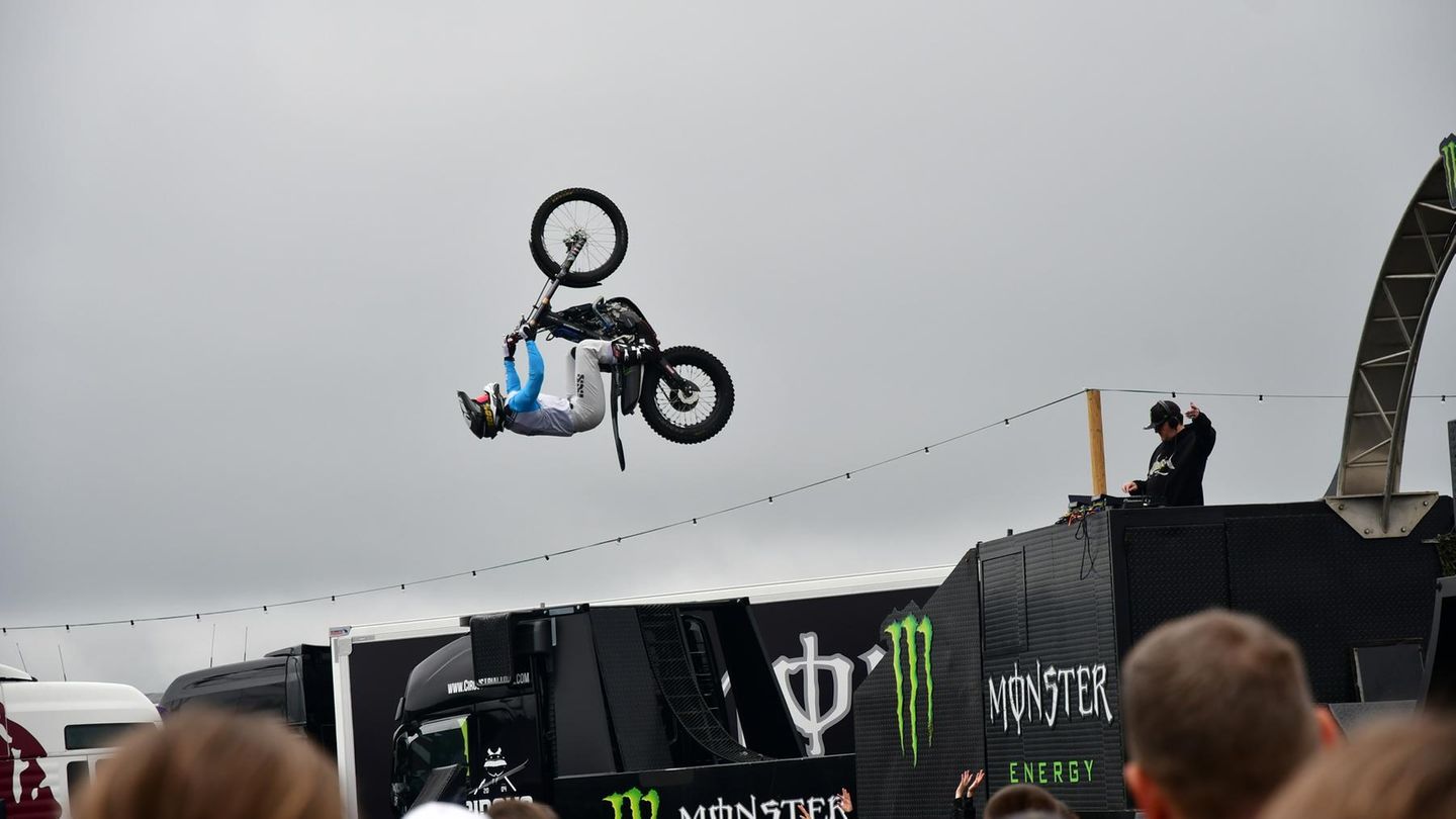 Im Fahrerlager tobt die große Show von Monster Energie. Zwei Motorrad Artisten fliegen mit ihren Maschinen durch die Luft, Girls klatschen Beifall und heiße Musik dröhnt aus den Boxen.
