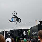 Im Fahrerlager tobt die große Show von Monster Energie. Zwei Motorrad Artisten fliegen mit ihren Maschinen durch die Luft, Girls klatschen Beifall und heiße Musik dröhnt aus den Boxen.