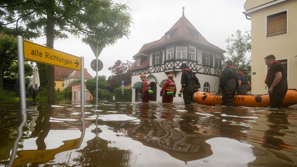 Feuerwehrleute und Wasserretter waten durch eine überflutete Straße.