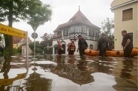 Feuerwehrleute und Wasserretter waten durch eine überflutete Straße.