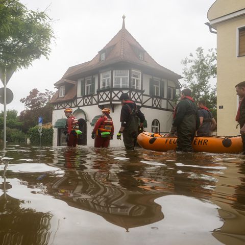 Feuerwehrleute und Wasserretter waten durch eine überflutete Straße.