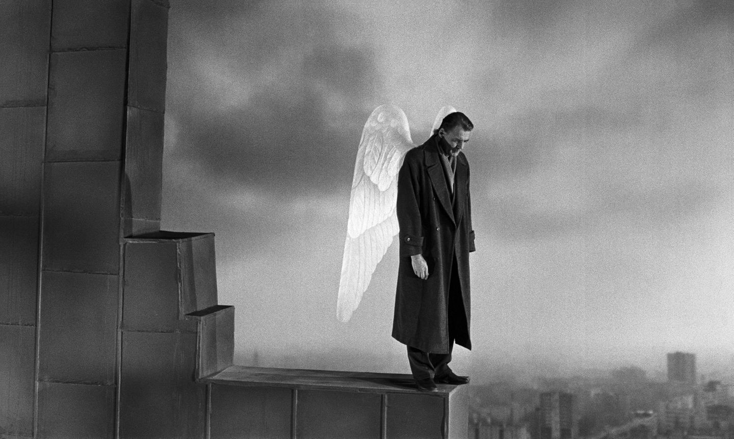 Ein Mann mit Mantel und Engelsflügeln steht an eiem Abgrund und schaut nach unten.
