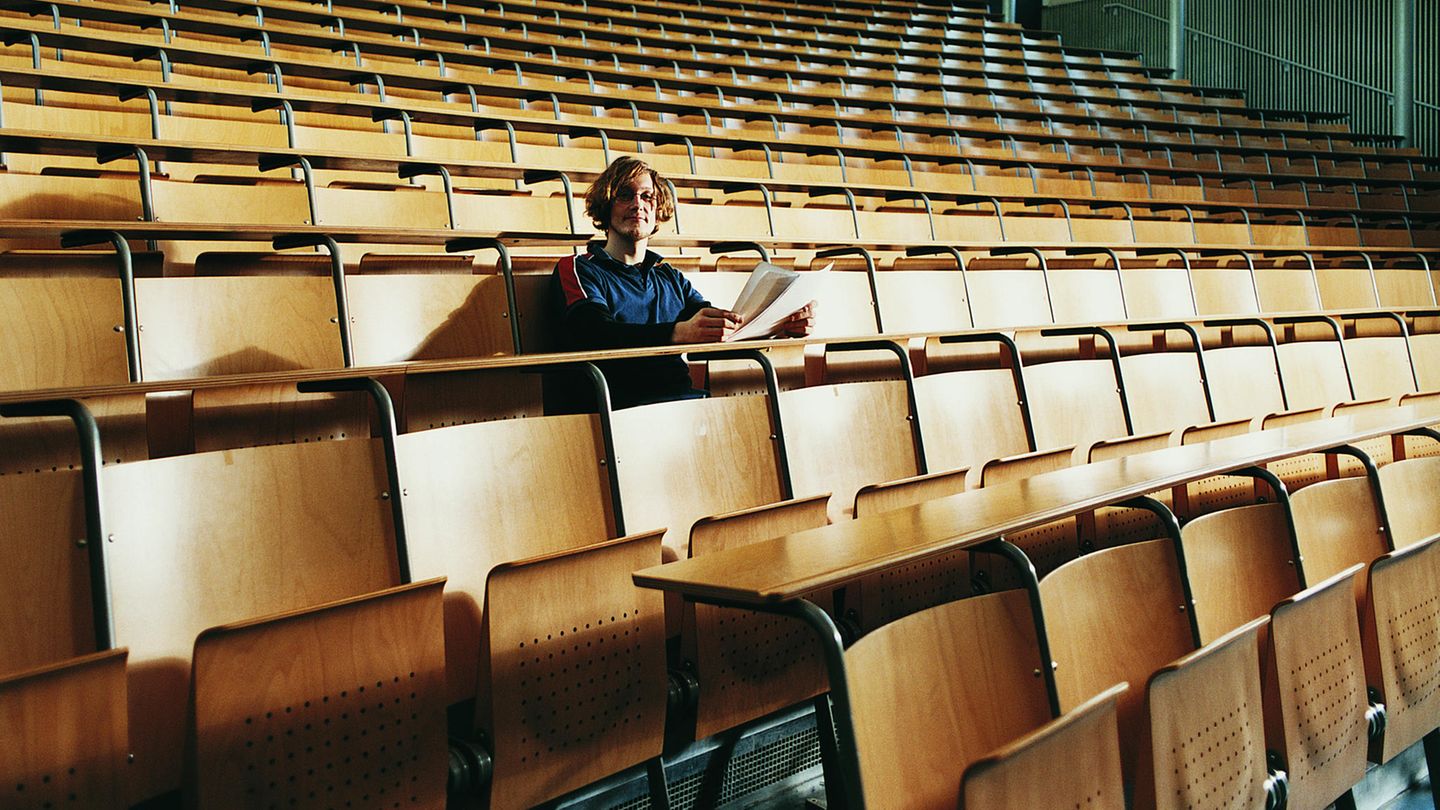 Symbolbild Intelligenz: Ein junger Mann sitzt alleine mit Zetteln in der Hand in einem Hörsaal