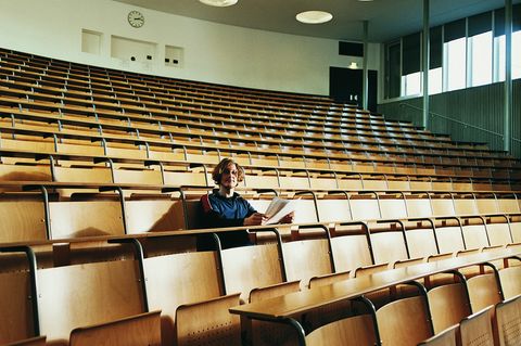 Symbolbild Intelligenz: Ein junger Mann sitzt alleine mit Zetteln in der Hand in einem Hörsaal