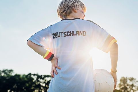 Ein kleiner junge in Deutschland-Trikot, mit schwarz-rot-goldenem Schweißband und Fußball
