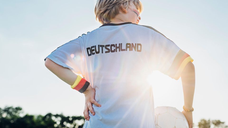 Ein kleiner Junge im Deutschlandtrikot, mit schwarz-rot-goldenem Schweißband und einem Fußball