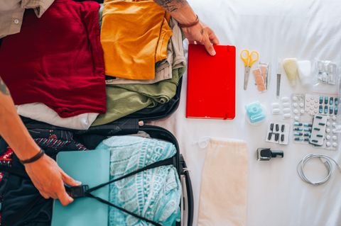 Krank im Urlaub: Aufgeklappter Koffer mit vielen Medikamenten daneben