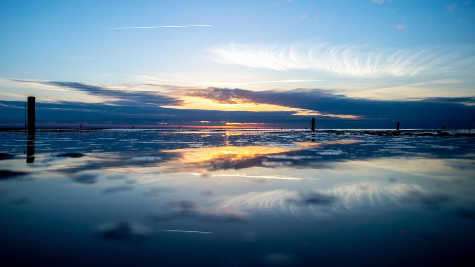 Die Sonne geht über der Nordsee auf Norderney unter und spiegelt sich dabei in einem Priel