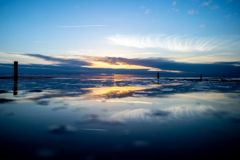 Die Sonne geht über der Nordsee auf Norderney unter und spiegelt sich dabei in einem Priel