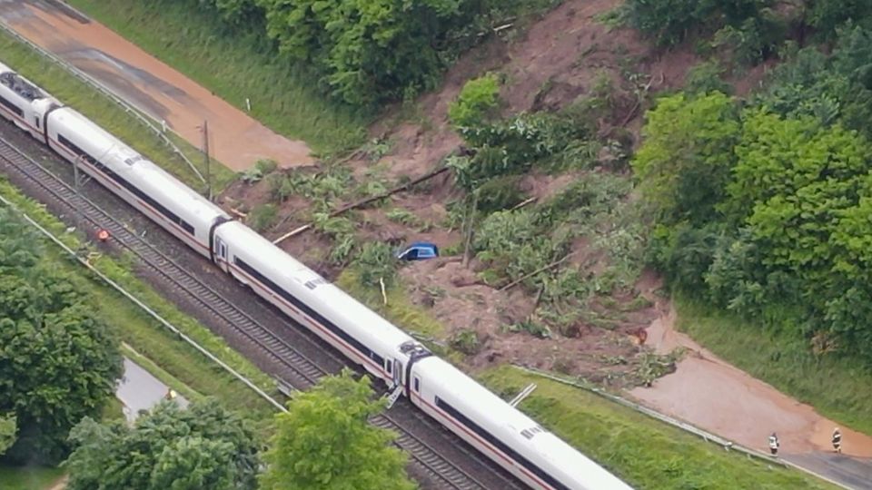 Ein Zug in der Hochwasser-Region liegt an einem Berghang, daneben ein Auto, überall ist schlamm.