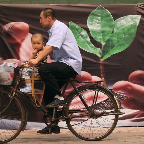 Ein Mann mit Kleinkind radelt an einem Plakat in China vorbei