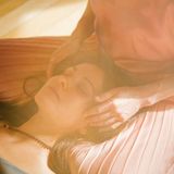 Eine Frau liegt mit geschlossenen Augen mit ihrem Kopf im Schoß einer anderen und wird am Kopf berührt