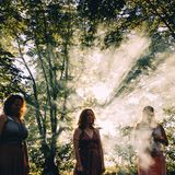 Frauen stehen um ein Feuer, das Licht der Sonne, das durch die Baumkronen fällt, erzeugt strahlen im Rauch des Feuers