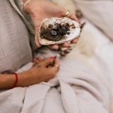 Eine Frau hält eine Muschelschale mit verbrannten Kräutern und Erde für ein Räucher Ritual in der Hand