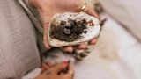 Eine Frau hält eine Muschelschale mit verbrannten Kräutern und Erde für ein Räucher Ritual in der Hand