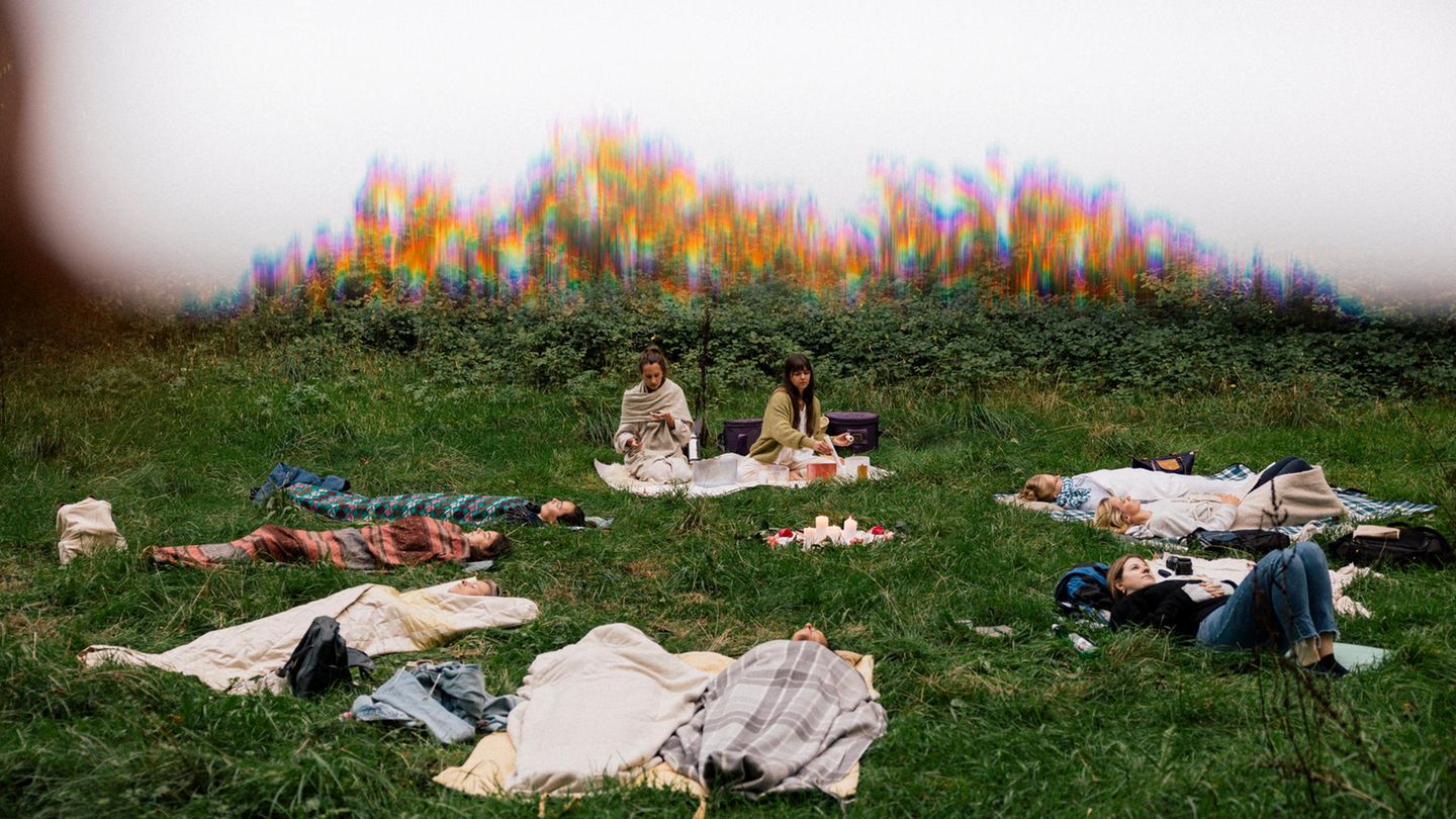 Frauen liegen auf einer Wiese in einem Kreis und machen eine geführte Meditation