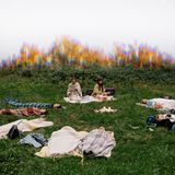 Frauen liegen auf einer Wiese in einem Kreis und machen eine geführte Meditation