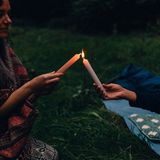 Eine Frau zündet eine weiße Kerze an einer Kerze einer anderen an