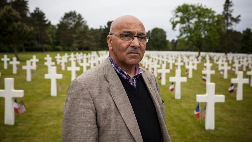 Priester Daniel Lefrançois vor Reihen weißer Kreuze auf einem Soldatenfriedhof in der Normandie