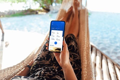 Eine Frau liegt im Urlaub in einer Hängematte und checkt ihre Rückreise daten