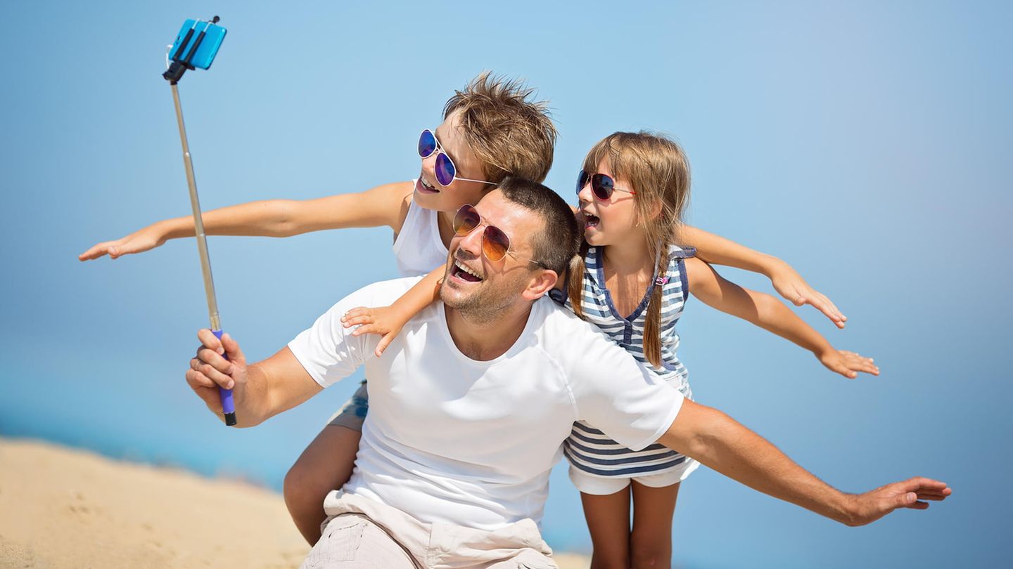 Vater benutzt Handy mit Selfiestick, um ein Foto zu machen