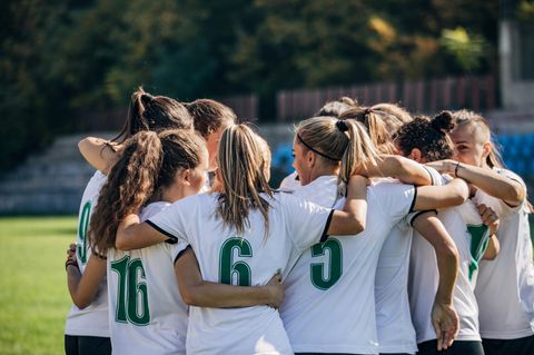 Frauen in Fußball-Trikots stehen Arm in Arm zusammen