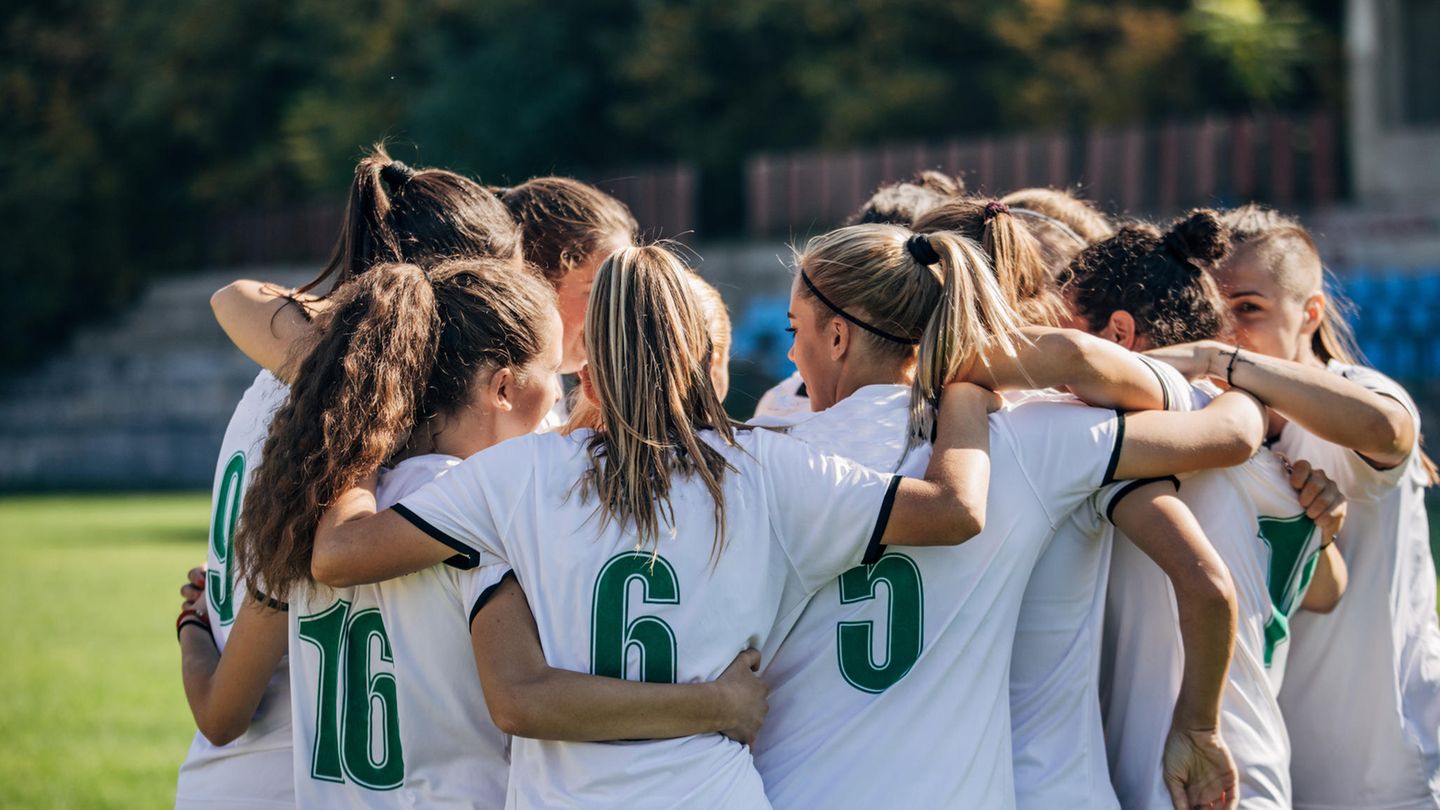 Frauen in Fußball-Trikots stehen Arm in Arm zusammen