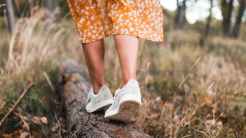 Eine Frau trägt nachhaltige Schuhe und balanciert auf einem Baumstamm.