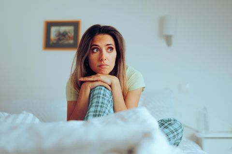 Eine Frau sitzt im Bett, stützt das Kinnd auf und guckt zur Seite
