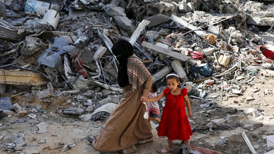 Eine Frau und ein Kind laufen durch die Trümmer eine Flüchtlingscamps im Gazastreifen.