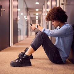 Eine junge Frau sitzt auf einem Flur in einem Büro auf dem Boden und schaut frustriert