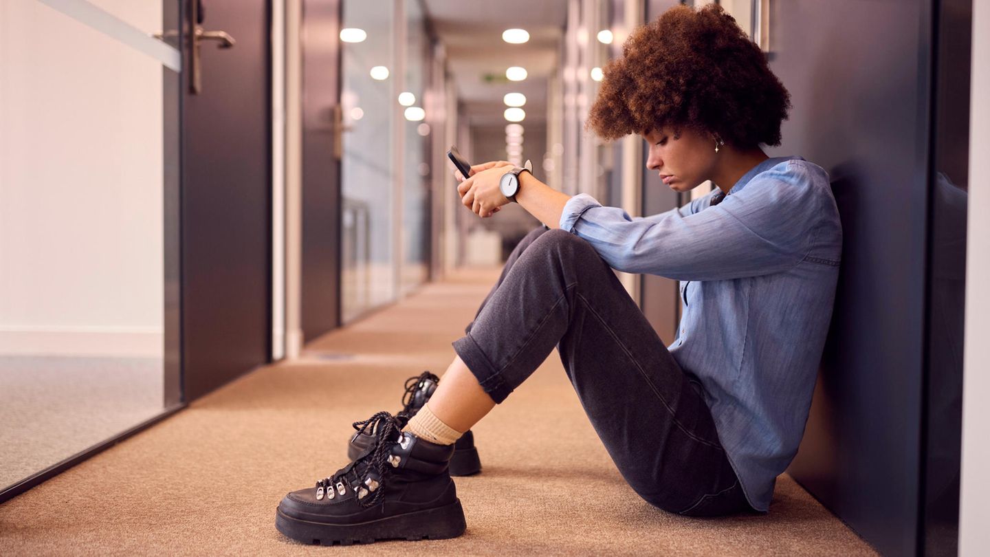 Eine junge Frau sitzt auf einem Flur in einem Büro auf dem Boden und schaut frustriert